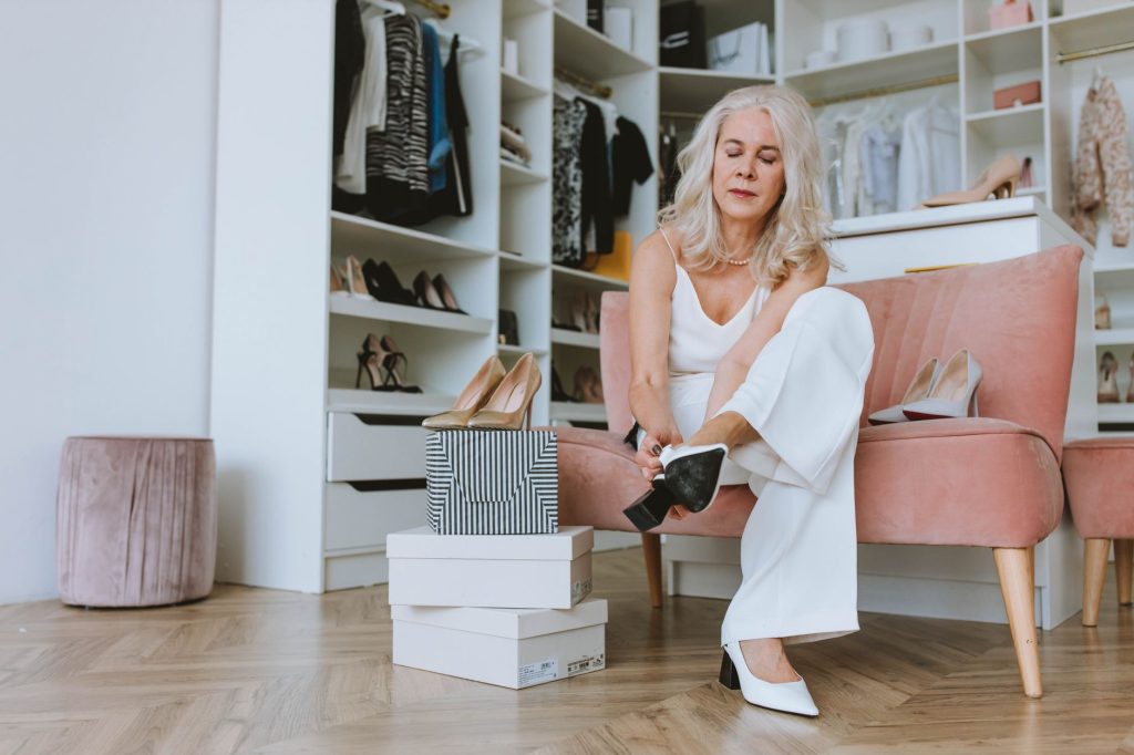 Femme assise dans son dressing qui essaie un escarpin, boîtes à chaussures posées à côté
