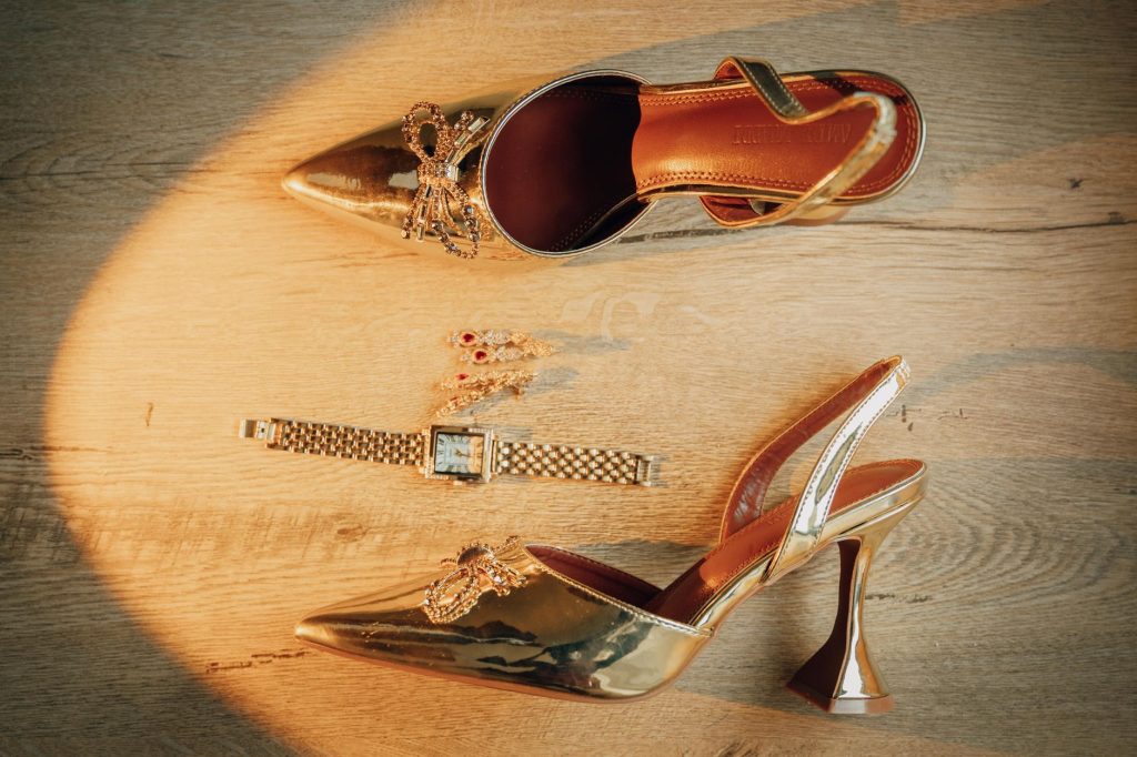 Mules dorées à petit talon posées sur un parquet, à côté d’une montre dorée