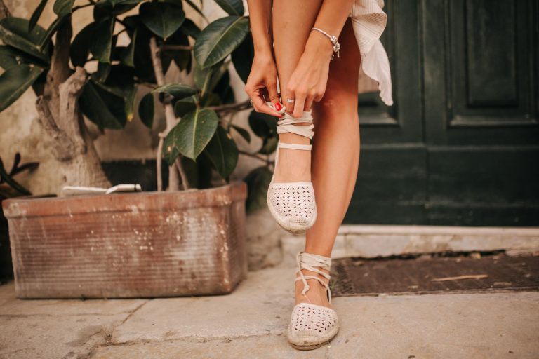 Femme qui noue ses espadrilles à lacets devant une porte