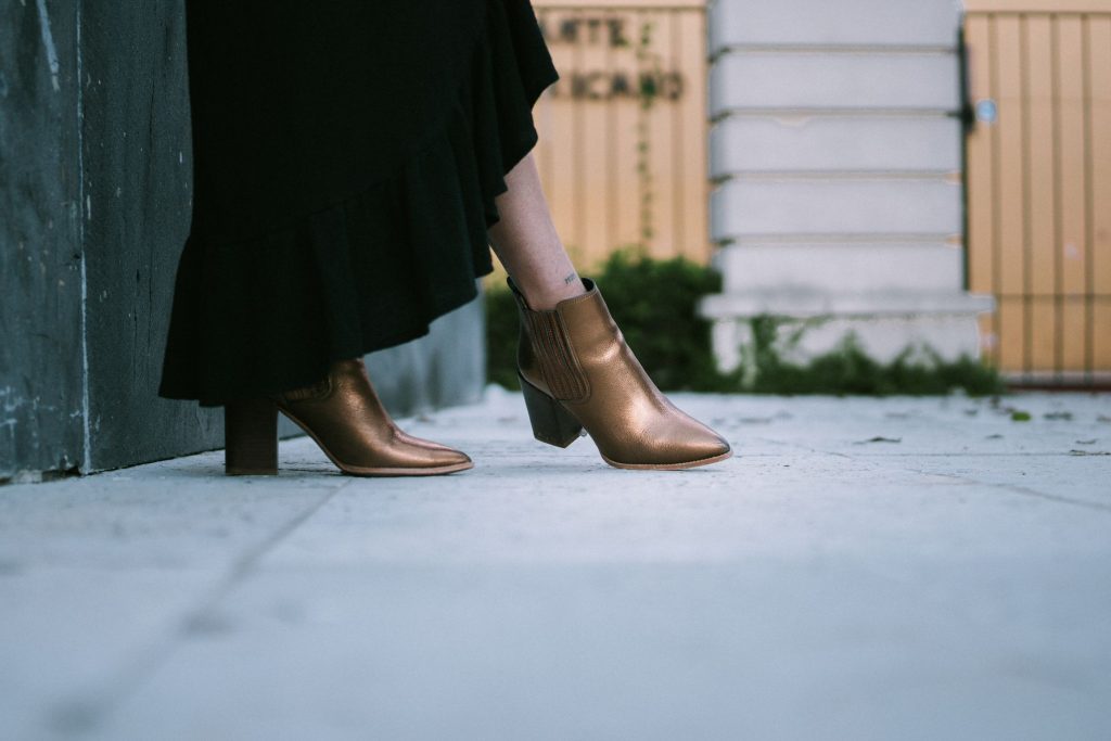 Robe longue noire et bottines à talon bloc couleur bronze sur un trottoir